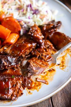 a white plate topped with meat and veggies next to coleslaw on a wooden table