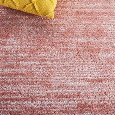 a yellow pillow sitting on top of a pink rug next to a red and white carpet