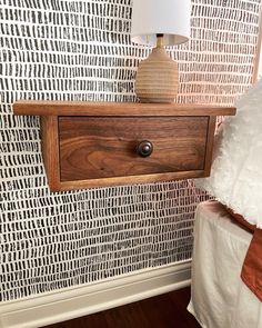 a nightstand with a lamp on top of it next to a wallpapered wall