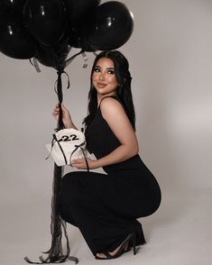 a woman kneeling down holding some black balloons in her hand and posing for the camera