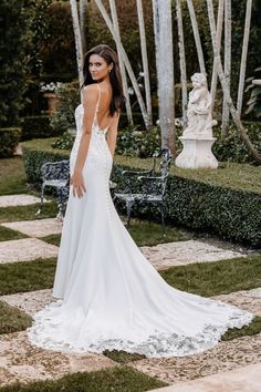 a woman in a white wedding dress standing on the grass with her back to the camera