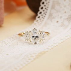 three stone ring sitting on top of a white lace table cloth next to a vase