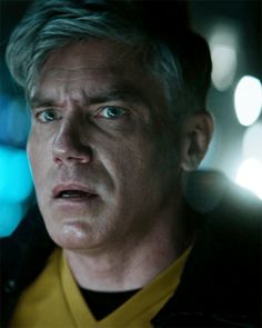 a man with grey hair wearing a yellow shirt and black jacket looking at the camera