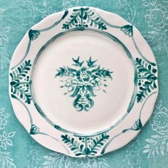 a white and blue plate with green designs on it sitting on a turquoise table cloth