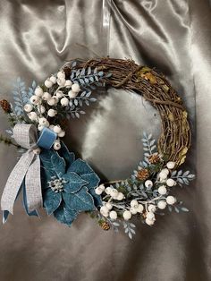 a wreath with white flowers and blue leaves on a silver satin background, ready to be used as an ornament