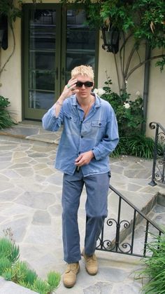 a man in blue shirt and pants standing on steps with sunglasses on his head while talking on cell phone