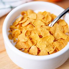 a white bowl filled with corn flakes on top of a wooden table next to an orange