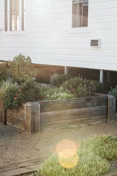 a wooden planter filled with lots of plants next to a white house