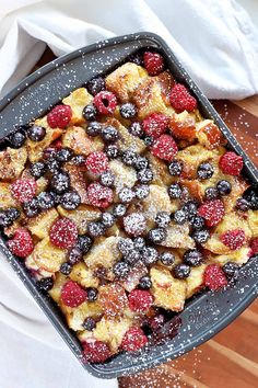 a pan filled with french toast and berries on top of a wooden table next to a white towel