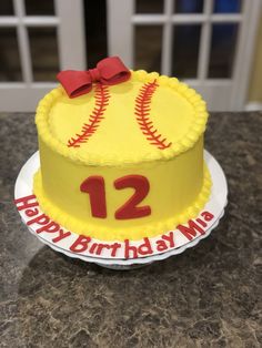 a baseball themed birthday cake with the number twelve on it and a red bow is sitting on a table