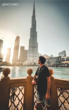 a man standing on top of a bridge next to a body of water with tall buildings in the background