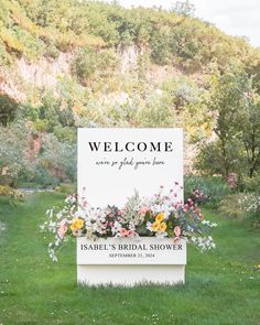 a welcome sign in front of a lush green field with flowers and greenery on it