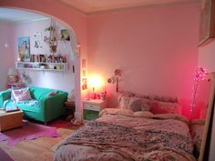 a bed room with a neatly made bed next to a green couch and pink walls