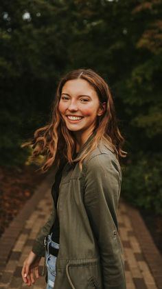 a woman standing on a brick path in front of some trees and smiling at the camera