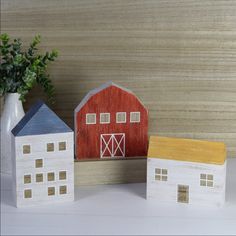 three small wooden houses sitting next to each other on a white counter top with a vase and potted plant in the background