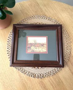 a wooden table with a framed painting on it and a potted plant next to it