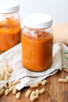 two jars filled with sauce sitting on top of a wooden table next to pasta shells