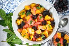 a white bowl filled with fruit and vegetables next to two spoons on top of a table