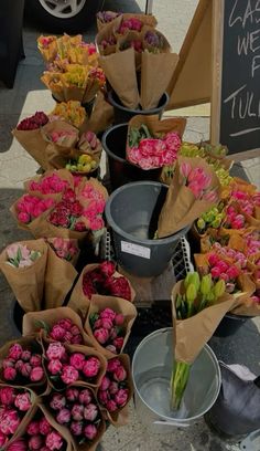 several buckets filled with flowers sitting next to each other on the ground in front of a sign