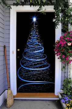 a lighted christmas tree on the front door of a house with flowers and brooms