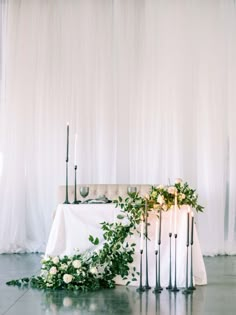 the table is set up with candles and greenery for an elegant wedding reception in front of white drapes