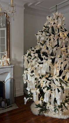 a decorated christmas tree with white bows and lights in a living room next to a fireplace