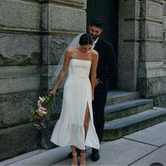 a bride and groom are standing on the sidewalk