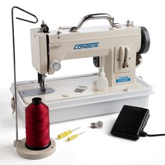 a sewing machine sitting on top of a white table next to a red thread spool