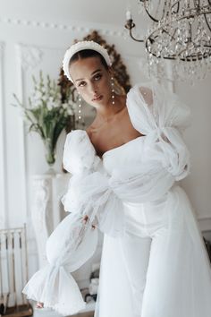 a woman in a white dress is standing near a chandelier