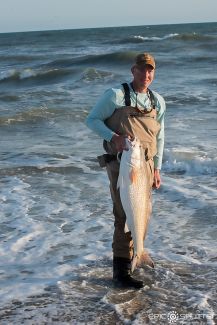 a man standing in the ocean holding a fish