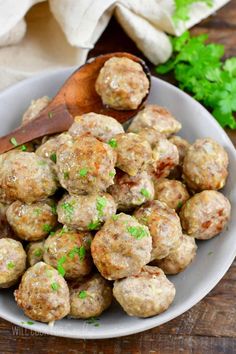 a white bowl filled with meatballs on top of a wooden table next to parsley