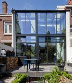 an outdoor dining area in front of a large building with lots of windows and plants