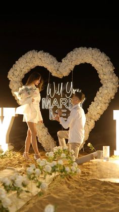 two people standing in front of a heart shaped sign