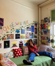 a woman sitting on top of a bed next to a wall covered in pictures and plants