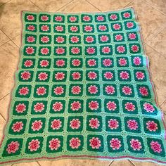 a green crocheted blanket with pink flowers on it sitting on the floor next to a tile floor