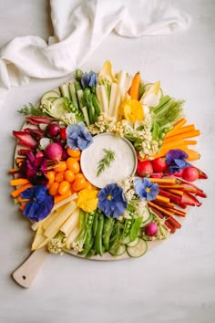 a platter filled with vegetables and dip surrounded by other food items on a white surface