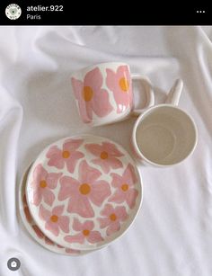 two cups and saucers are sitting on a white sheet with pink flowers painted on them