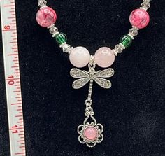 a necklace with pink, green and white beads is displayed in front of a ruler