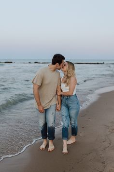 a man and woman kissing on the beach with waves coming in from the ocean behind them