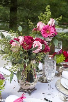 the table is set with pink and red flowers in vases, silverware, and wine glasses