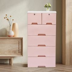 a pink chest of drawers next to a vase with flowers