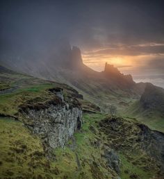 the sun is setting over some mountains and grass in the foreground, with an old stone wall leading up to it