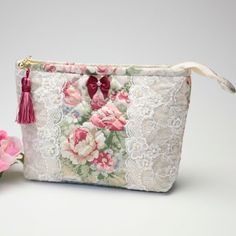 a white lace pouch with pink flowers and a tassel on the side, sitting next to it