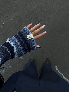 a person with their hand in a knitted mitt on the street, looking down at them