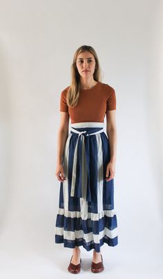 "DETAILS ◦ Vintage 1970s maxi/ankle length skirt ◦ Vertical white and navy blue stripe, horizontal on bottom ◦ Wide waistband with ties at waist ◦ Ruffled, gathered bottom ◦ Center back zipper ◦ Texture on fabric - fabric is sheer will need a slip (slip not included) ◦ Please note: Not sure how the ties are tied on skirt! There is a small opening on waistband where I assume the strap is supposed to go through. Labeled S Estimated Size | W 24\" Measurements | Waist - 24\" Hips - open Skirt Length Blue Ruffled Maxi Skirt, Blue Gathered Midi-length Maxi Skirt, Blue Midi Length Gathered Maxi Skirt, Texture On Fabric, Open Skirt, White Striped Skirt, Ankle Length Skirt, Hip Openers, Striped Skirt