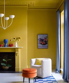 a living room with yellow walls and blue drapes on the window sill, white chair, and fireplace