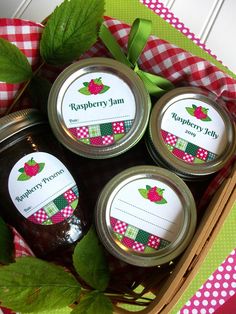 four jars of jam sitting on top of a table next to green leaves and gingham cloth