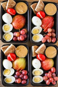 four black trays filled with different types of food on top of a wooden table