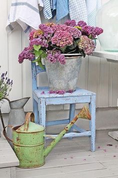 an old blue chair with flowers on it and a watering can next to the chair