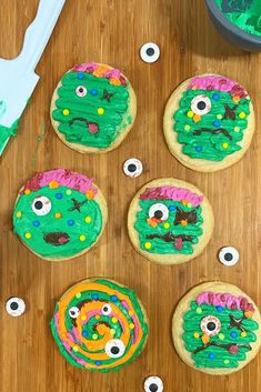 decorated cookies sitting on top of a wooden table next to green frosting and googly eyes